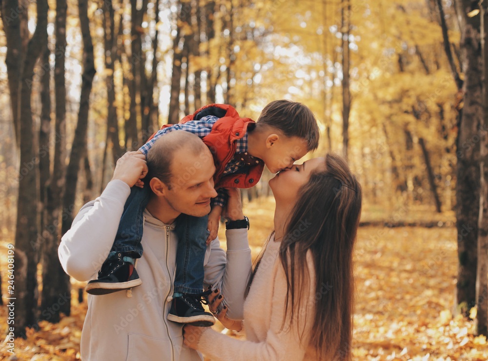 Little child sitting on father's shoulders. Mother kisses her son Little child sitting on father's shoulders. Mother kisses her son