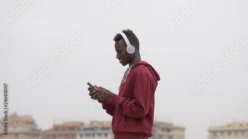 young african american guy listening music and typing on smartphone-outdoor photo