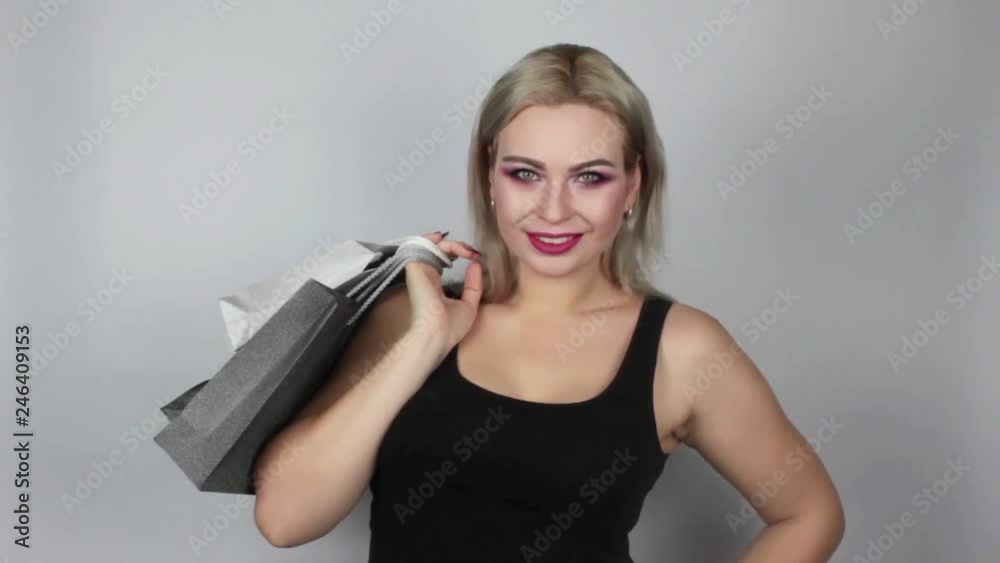 Female shopper holding shopping bags on grey background in studio.