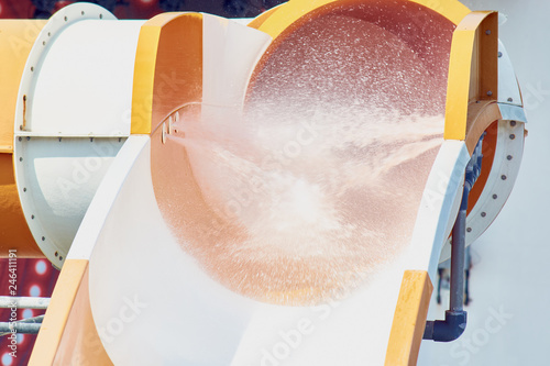 The stream of splashing water on waterslide in water park for riding children.