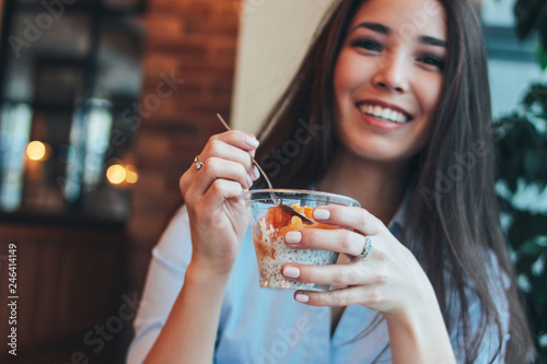 Beautiful charming brunette smiling Asian girl has Breakfast with coffee and Chia pudding at cafe