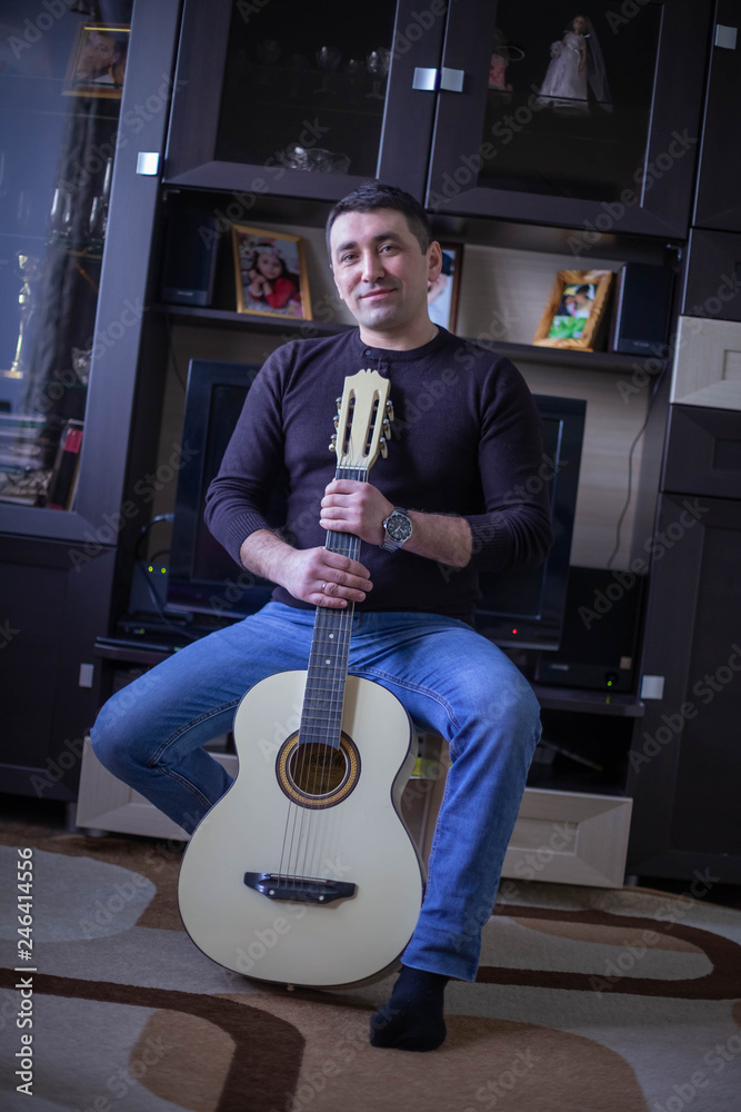 Fototapeta a man in a black t-shirt and blue jeans with a guitar in the interior of the apartment
