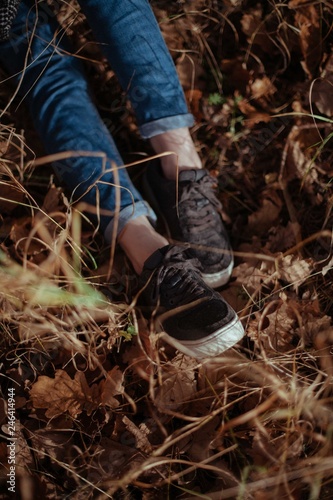 Women's legs in jeans and sneakers in the dry grass