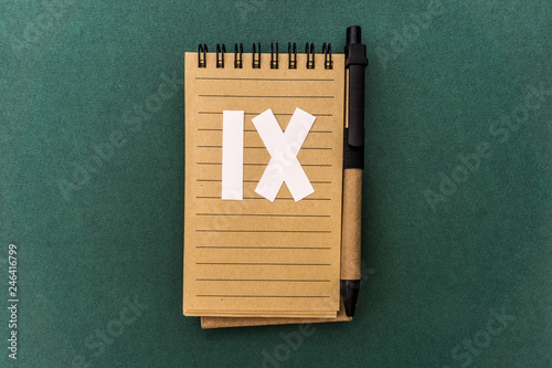 Notebook front with pen and white nine  Roman number on green background. Spiral notepad on a table. Nine, 9 chapter, September.