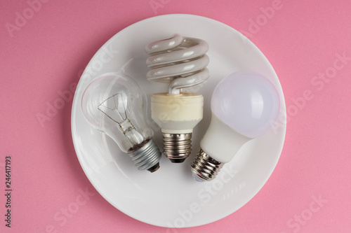 Incandescent lamp, fluorescent lamp and LED lamp in metaphor on technological progress on pink background