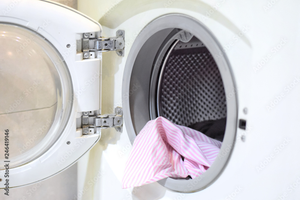 White washing machine with steel circle drum in bathrooms with pink cotton shirt inside. Dirty colorful clothes loading in electrical washing machine. Laundry home work. Laundering chore. White washing machine with steel circle drum in bathrooms with pink cotton shirt inside. Dirty colorful clothes loading in electrical washing machine. Laundry home work. Laundering chore.