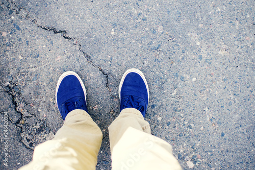 Male legs in blue sneakers on asphalt road, top view.