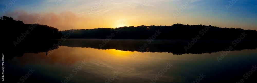 Panoramic view of the rising sun peeks over the foggy horizon at Shelley Lake Park in Raleigh North Carolina.