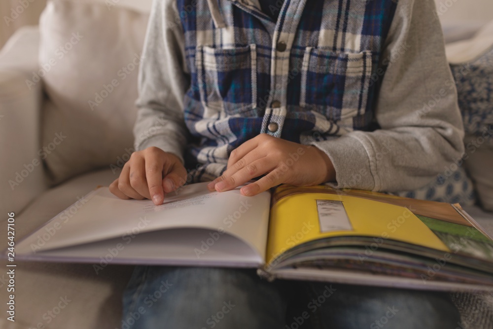 Mid section of boy reading a story book in living room Mid section of boy reading a story book in living room