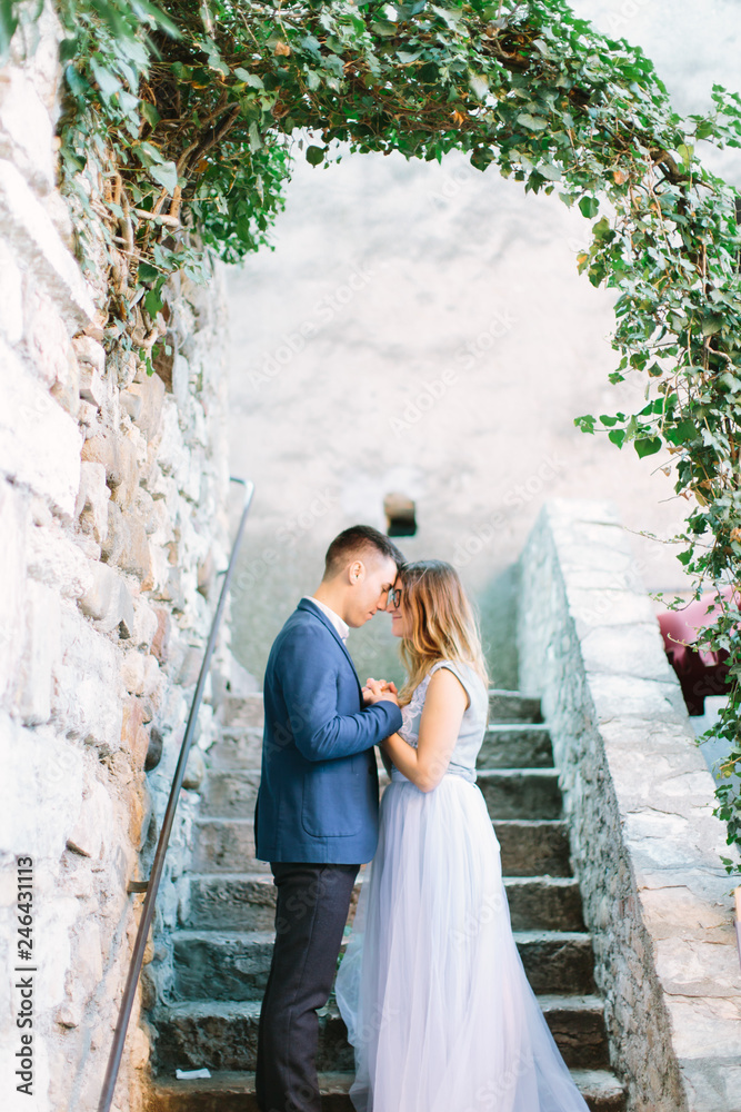 young beautiful couple in blue clothes posing and keeping hands together while standing on the ancient stairs in old town Sirmione, Italy