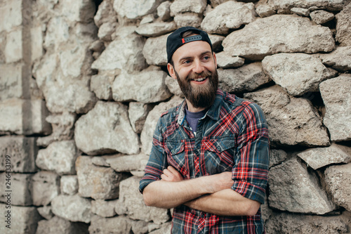 Portrait of young handsome hipster man with beard laughing over stone wall