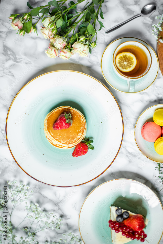 pancakes with tea, cheesecake and biscuits on a marble table with flowers pancakes with tea, cheesecake and biscuits on a marble table with flowers
