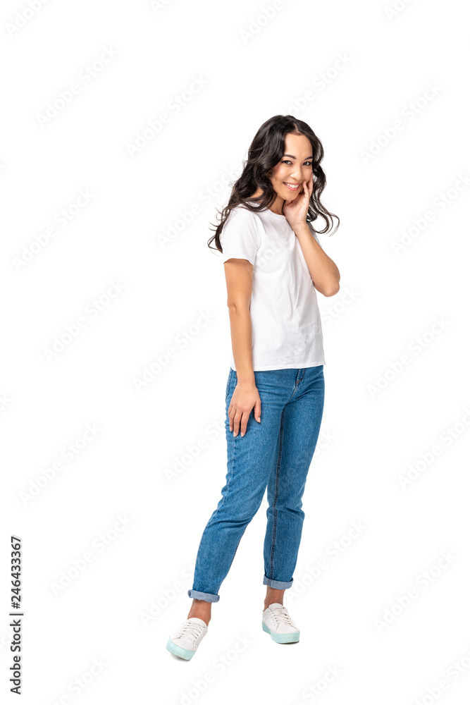 Shy asian woman in white t-shirt and blue jeans holding hand near face isolated on white Shy asian woman in white t-shirt and blue jeans holding hand near face isolated on white