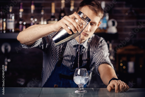 Barman prepares cocktail in shaker with alcohol and ice. Dark background Bartender