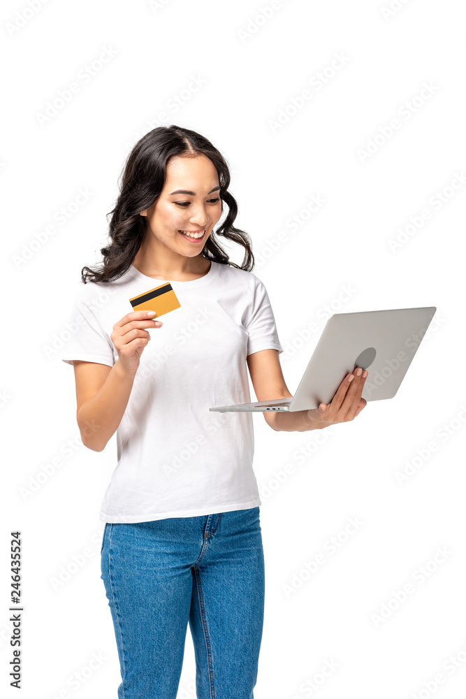 Smiling pretty asian woman in white t-shirt and blue jeans using laptop and holding credit card isolated on white Smiling pretty asian woman in white t-shirt and blue jeans using laptop and holding credit card isolated on white