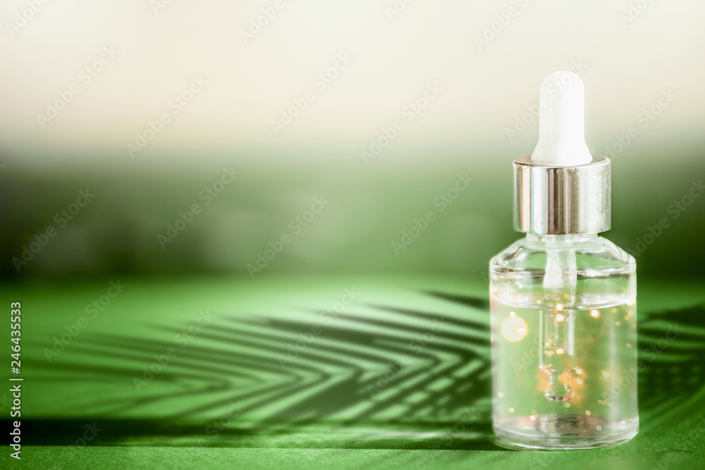 Transparent cosmetic bottle with pipette standing on green table with palm leaves shadow. Facial skin care concept. Natural vegan cosmetic. Serum or skin essential oil. Modern beauty trend. Transparent cosmetic bottle with pipette standing on green table with palm leaves shadow. Facial skin care concept. Natural vegan cosmetic. Serum or skin essential oil. Modern beauty trend.