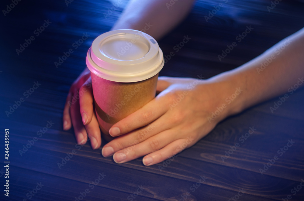 A cup of coffee on a wooden table in female hands. Paper cup Plastic cap Beautiful hands Girl bar counter light A cup of coffee on a wooden table in female hands. Paper cup Plastic cap Beautiful hands Girl bar counter light