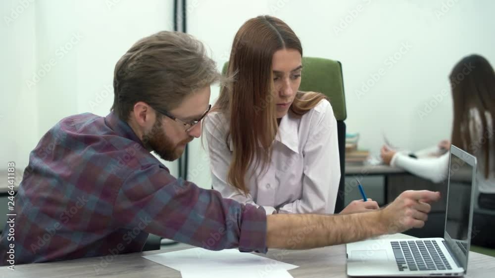 A bearded manager with glasses shares a new business strategy with his colleague showing on the laptop screen. Creative business team meeting in modern office. A bearded manager with glasses shares a new business strategy with his colleague showing on the laptop screen. Creative business team meeting in modern office.