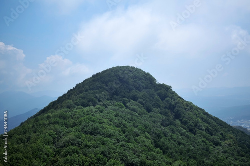 Mountain covered with forest against the blue sky with clouds