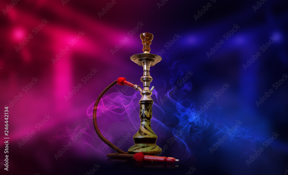 Smoking hookah on the background of an empty room. Multicolored neon light. Searchlight, laser blue and pink rays, smoke. Smoking hookah on the background of an empty room. Multicolored neon light. Searchlight, laser blue and pink rays, smoke.