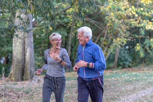 Aged couple jogging in park and smile
