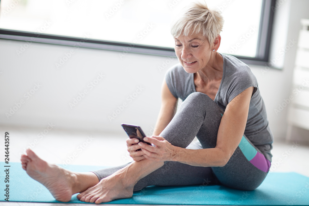 Modern short blonde hair mature woman using mobile phone while relax after  exercise in corner of room with window at background Stock Photo | Adobe  Stock