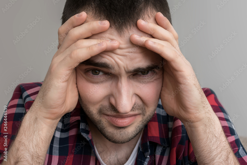 A male has a headache, squeezes his head with his hands, close up A male has a headache, squeezes his head with his hands, close up