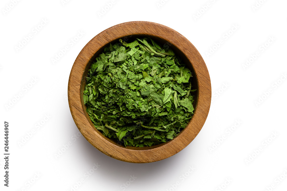 Dried chopped parsley in dark wood bowl isolated on white from above. Dried chopped parsley in dark wood bowl isolated on white from above.