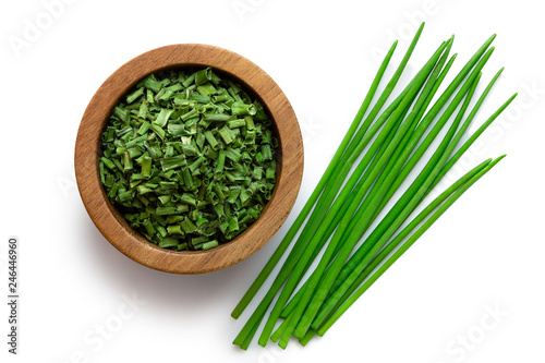 Dried chopped chives in a dark wood bowl next to a pile of whole fresh chives isolated on white from above. photo