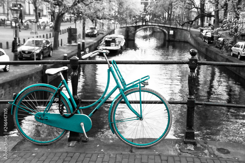 A picture of a lonely azure bike on the bridge over the channel in Amsterdam. The background is black and white. 