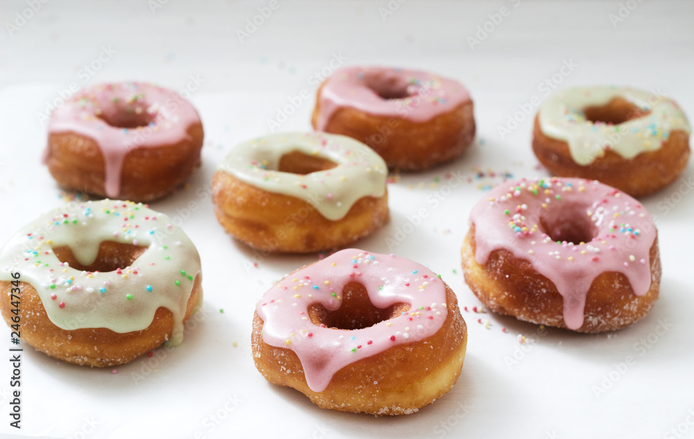 Homemade donuts decorated with colored icing and colored sugar on a light background.