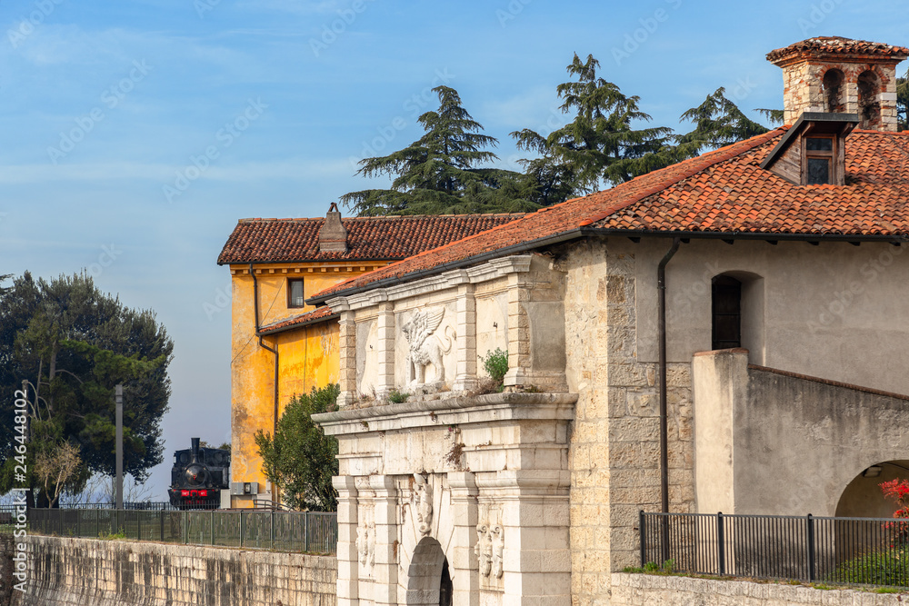 Fototapeta premium Entrance to the medieval castle of Brescia and an old locomotive installed in the park on the background, Lombardy, Italy
