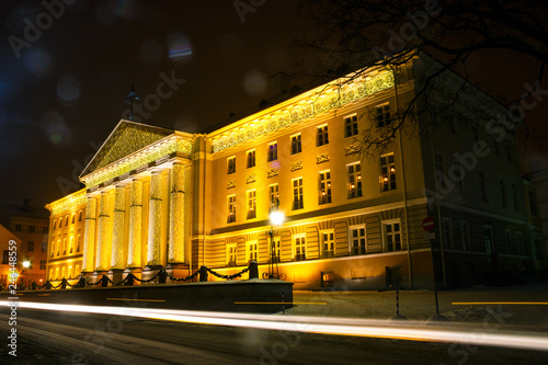 Facade of the main building of the University of Tartu, Estonia, in the Christmas decor on a winter evening. Trace from the car in the foreground.