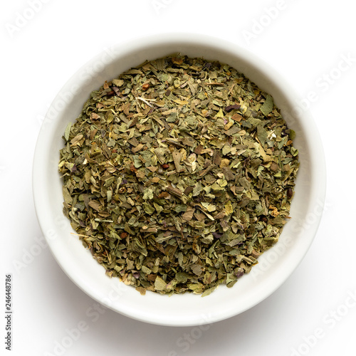 Dried chopped basil in white ceramic bowl isolated on white from above.