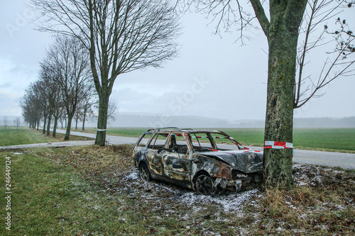 Car destroyed during the traffic accident. It was caused by the bad weather conditions in winter, because of the black ice or snow. The car is burnt, abandoned and stands by the road in the snowfall.