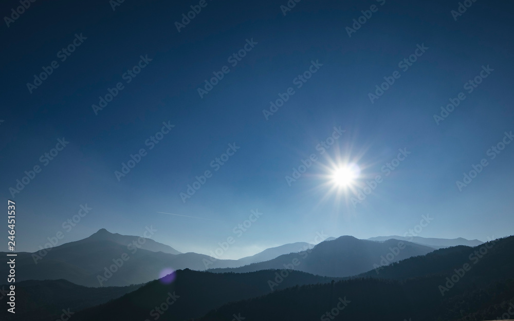 Sun shining over a solid blue sky on a mountain landscape