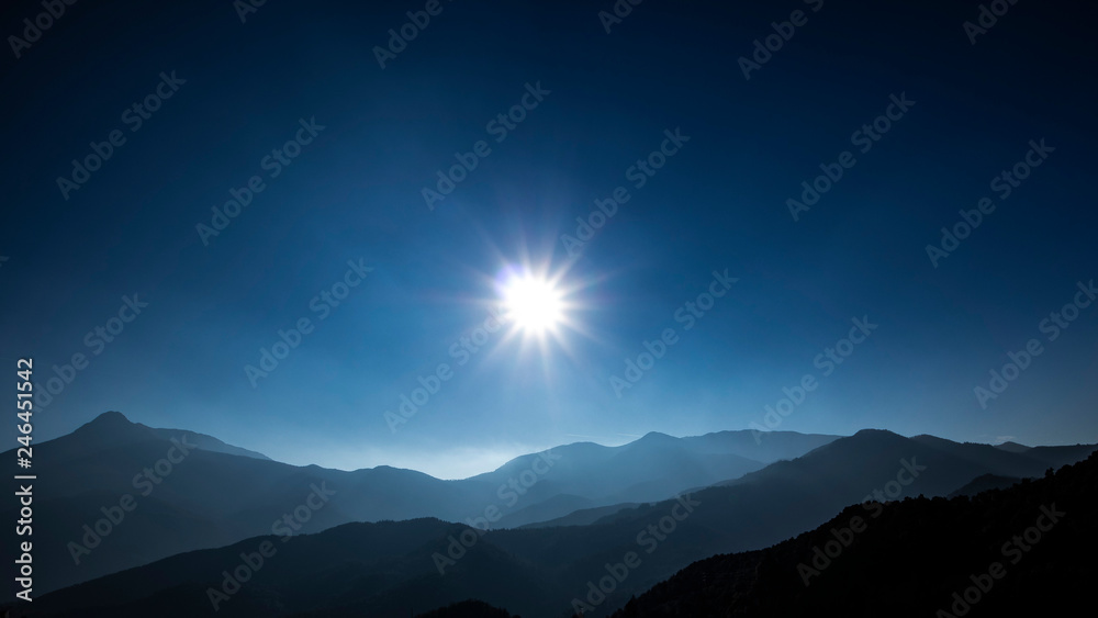 Sun shining over a solid blue sky on a mountain landscape