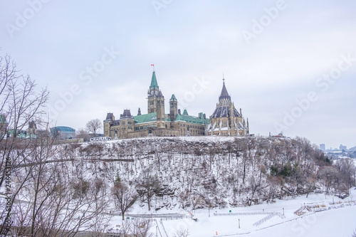 Scenic view of parliament of Canada building on bank of Ottawa river in Ontario in capital of country. Depressive beautiful winter look of old historic famous government building covered by snow