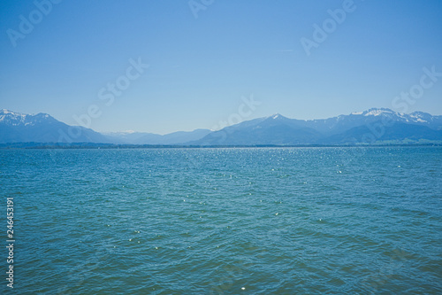 Blick über den sommerlichen Chiemsee in Richtung der Alpen mit blauem Himmel