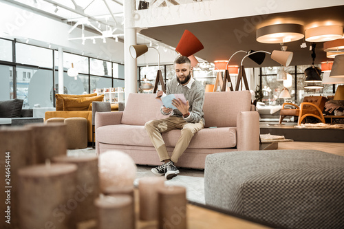 Curious bearded man observing catalog with variants of furniture