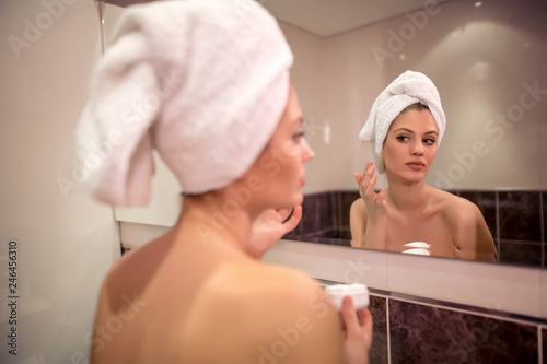 Beautiful woman applying cream on face