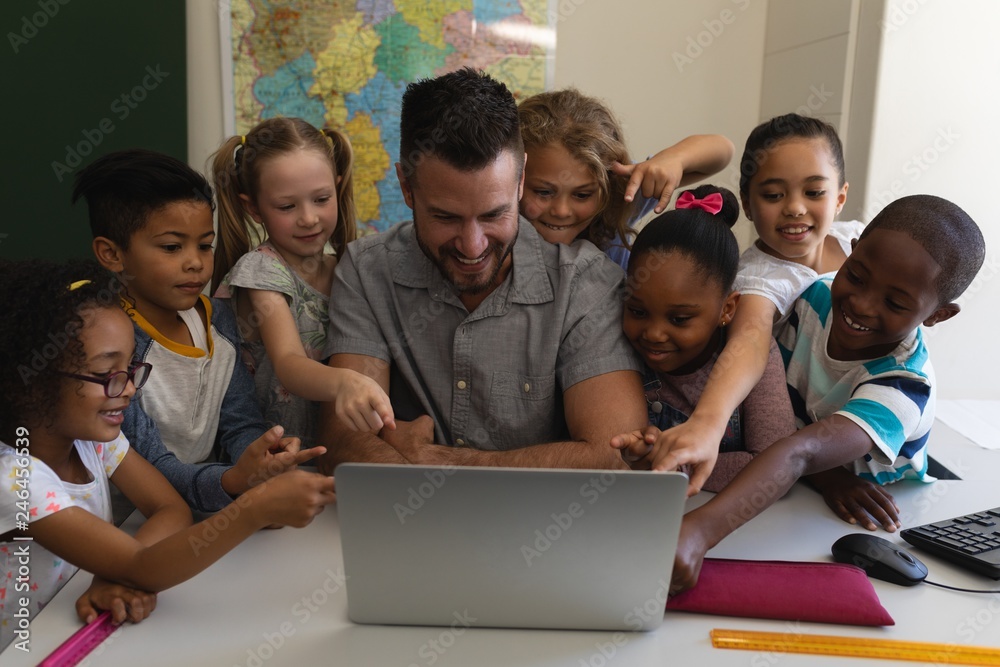 Male school teacher teaching schoolkid on laptop at desk in Male school teacher teaching schoolkid on laptop at desk in