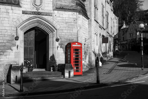 A traditional red British phone box is standing on the street of Bradford on Avon. The booth is isolated in a black and white picture. 