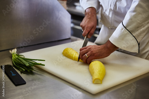 Chef slicing yellow squash on white cutting board photo