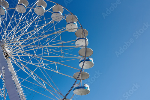 Underside view of ferris wheel in amusement park against clear blue sky.