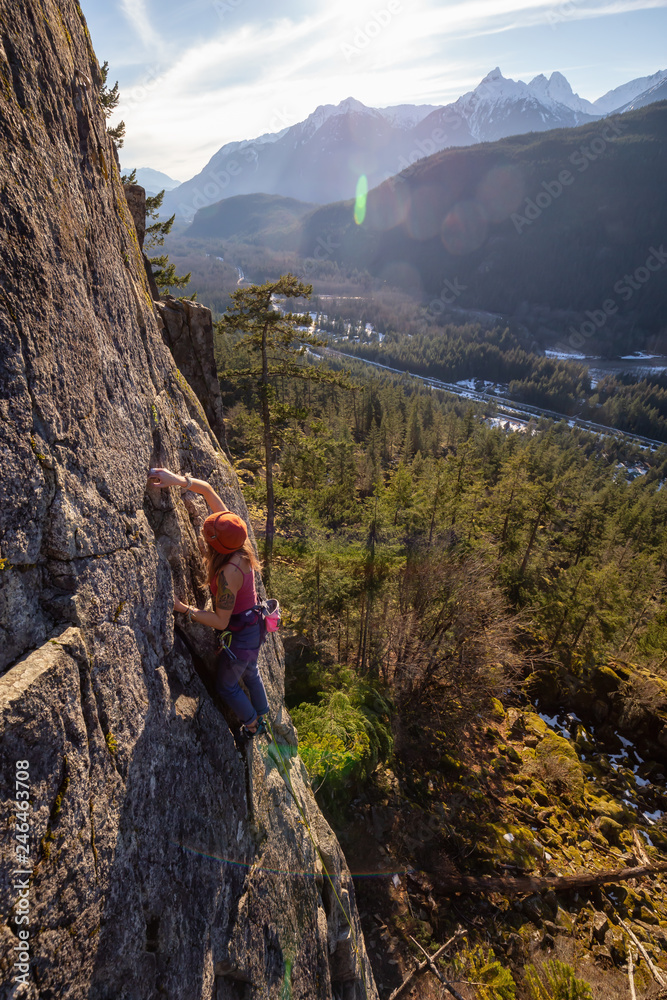 Squamish, BC, Canada - January 15, 2019: Female Rock climber climbing on the edge of the cliff during a sunny winter sunset.