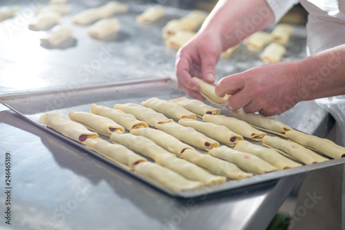 baker's female hands spread dough rolls on a tray for baking