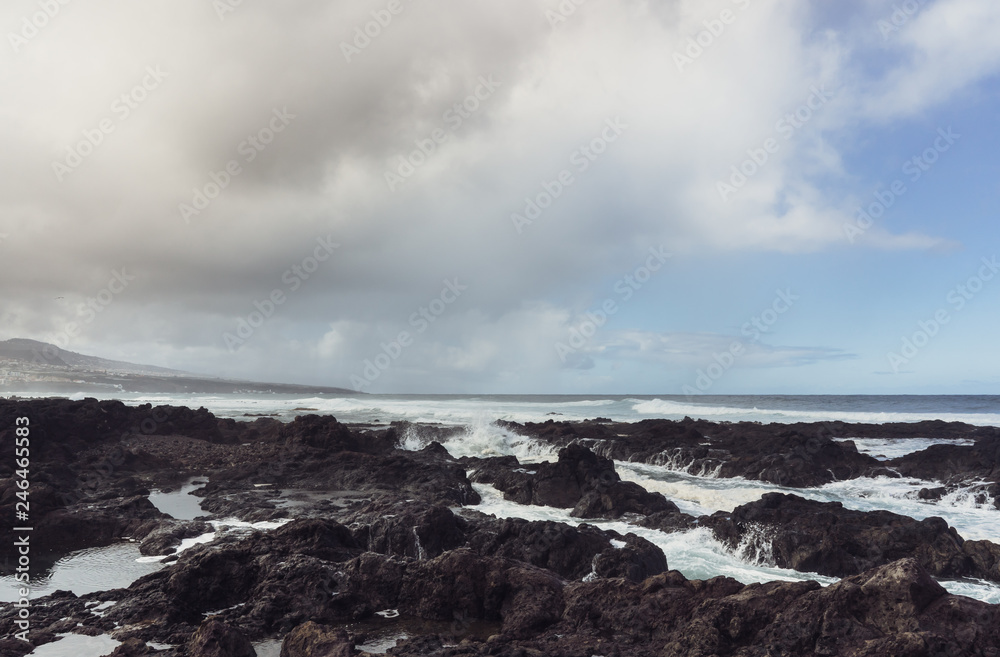 Punta del Hidalgo, Tenerife, Espania - October 27, 2018: Panorama of the rocky beach of Punta de Hidalgo and the waves breaking at the rocks, taken on a rainy day