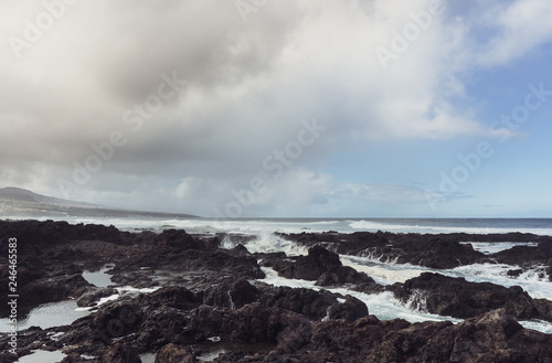 Punta del Hidalgo, Tenerife, Espania - October 27, 2018: Panorama of the rocky beach of Punta de Hidalgo and the waves breaking at the rocks, taken on a rainy day