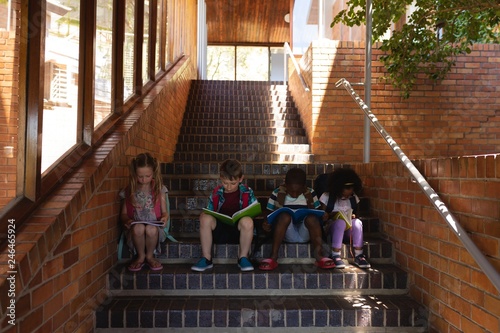 Schoolkids reading book while sitting on stairs of elementary